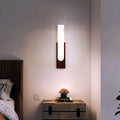 Applique murale longue effet albâtre et noyer allumée au-dessus d'une table de chevet