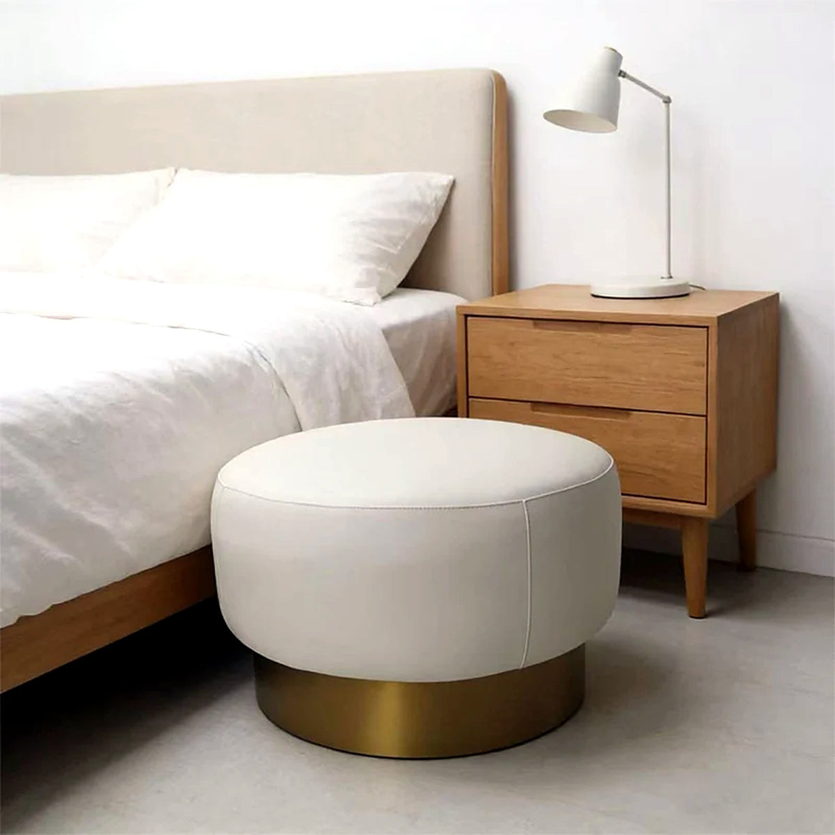 Pouf rond crème à socle doré brossé au pied d'un lit